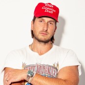 A man in a white graphic tshirt and red cap stood in front of a white wall